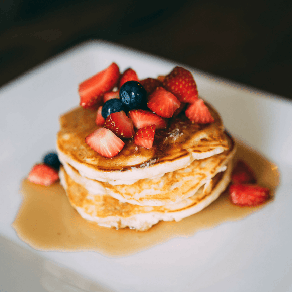 Stack of pancakes with syrup, strawberries and blueberries.